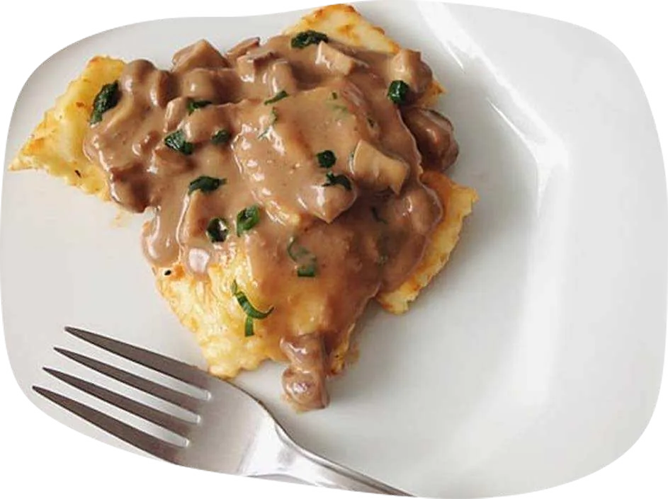 Massa recheada coberta com creme de portobello e salsinha, em prato branco com garfo.