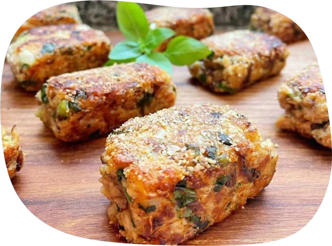 Nuggets de shitake dourados sobre tábua de madeira com folhas de manjericão.