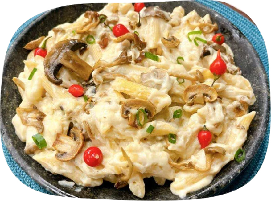 Macarrão em molho branco com cogumelos fatiados e pimentas vermelhas em frigideira.
